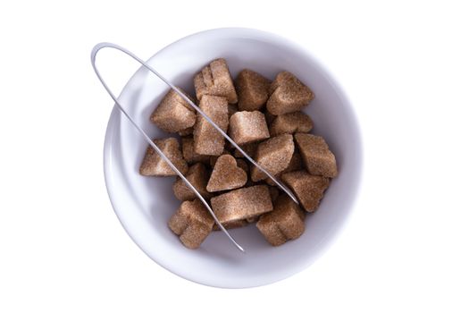 View from above of brown sugar cubes in a bowl with a pair of tongs for serving, isolated on white