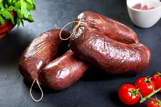 Uncooked fresh blood sausage with parsley and tomato. raw pork ready to cook black stone background