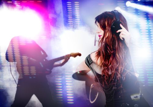 Beautiful woman listening to music with headphones. Live music background with guitar and bright lights on stage. Live music and party concept.