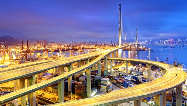 Container Cargo freight ship with working crane bridge in shipyard under Stonecutters highway bridge at sunset for Logistic Import Export, Hong kong