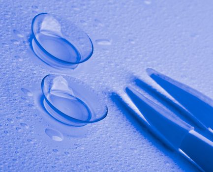 Arrangement of Two Contact Lenses with Water Droplets and Special Tweezers isolated on Wet background. Ultramarine Toned