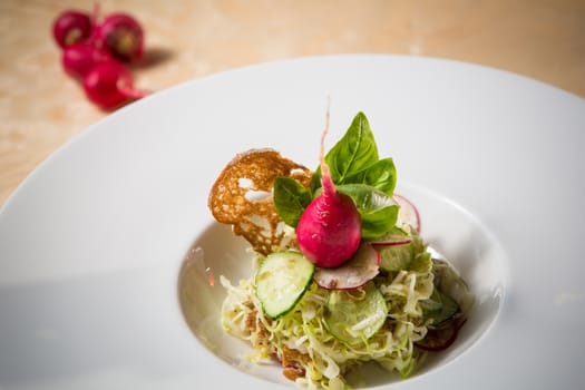 Salad from cabbage, herbs, cucumber, onion and radish in bowl on green wooden background. Coleslaw. Selective focus.