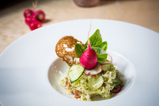 Salad from cabbage, herbs, cucumber, onion and radish in bowl on green wooden background. Coleslaw. Selective focus.