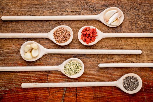 superfood abstract (garlic cloves, goji berry, chia, hemp, flax seeds, macadamia,nuts) - top view of wooden spoons against rustic grunge wood
