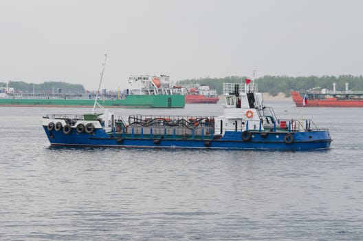 A small boat floats past standing in the roads tankers
