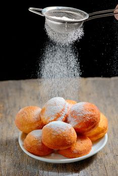 pours sugar with strainer over donuts 