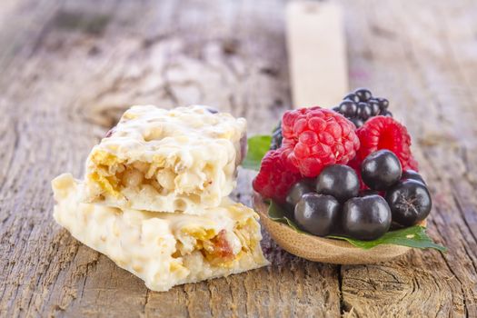 muesli bars with fresh berries in spoon on wooden background
