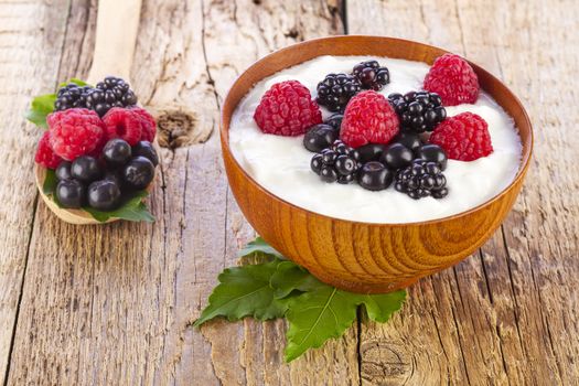 yogurt with wild berries in wooden bowl on wooden background