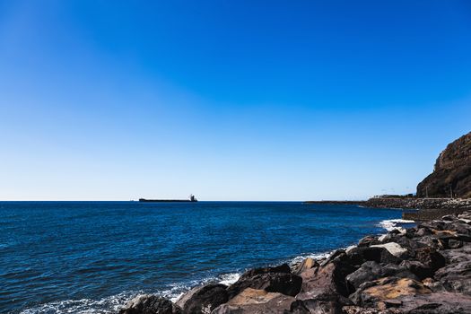 Empty container cargo ship in the open Atlantic ocean. View from stone coast or shore
