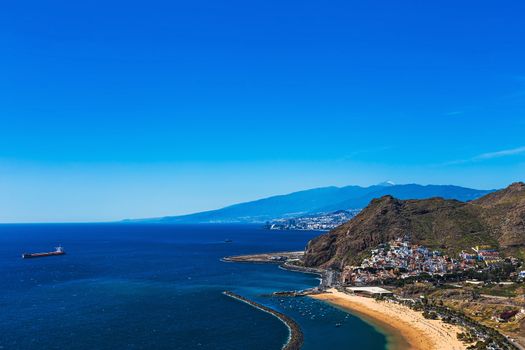 Santa Cruz city and beach or playa Las Teresitas on the coast of Atlantic ocean with ship on Tenerife Canary island, Spain at spring or summer. Teide volcano at background