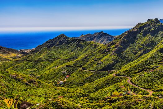 Green mountains or rocks valley with winding or serpantine road and sky with ocean on horizon landscape in Tenerife Canary island, Spain at spring
