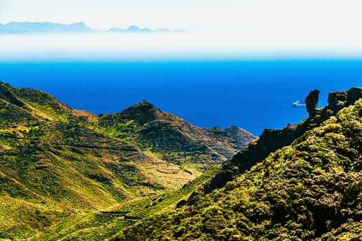 Coast or shore of Atlantic ocean with green mountain or rock with skyline and island in fog at background in Tenerife Canary island, Spain at spring or summer