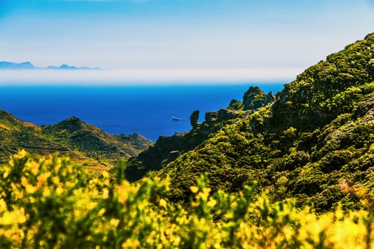 Coast or shore of Atlantic ocean with green mountain or rock and sky with horizon and island at background in Tenerife Canary island, Spain at spring or summer