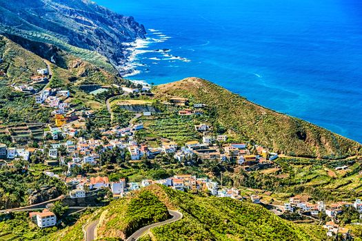 City or village buildings and winding or serpantine road in green mountain valley landscape near the shore of Atlantic ocean in Tenerife Canary island, Spain