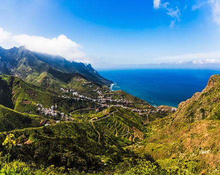 City or village buildings and winding or serpantine road in green mountain or rock valley and clouds horizon landscape near coast or shore of Atlantic ocean in Tenerife Canary island, Spain
