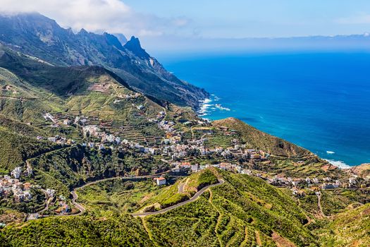 City or village buildings and winding or serpantine road in green mountain or rock valley and clouds with skyline landscape near shore of Atlantic ocean in Tenerife Canary island, Spain