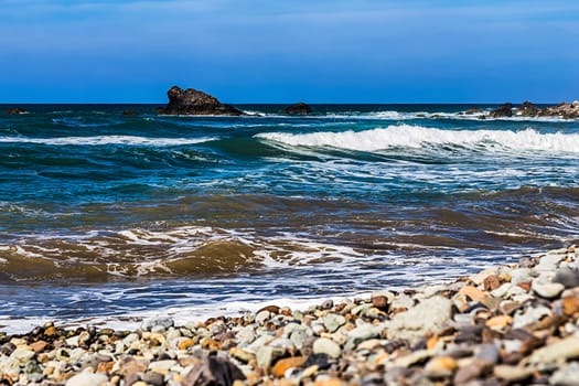Wild stone beach and rock in water on coast or shore of the Atlantic ocean with waves and sky with clouds and skyline or horizon in Tenerife Canary island, Spain at spring or summer