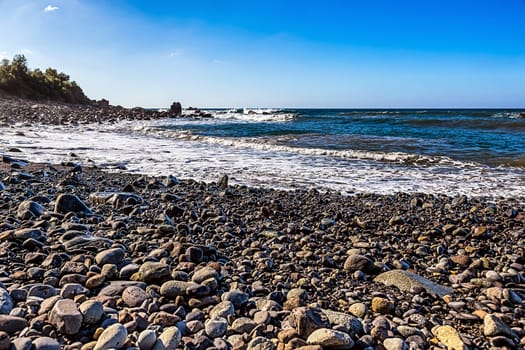 Wild stone beach on shore of the Atlantic ocean with waves and sky with clouds and skyline or horizon in Tenerife Canary island, Spain at spring or summer