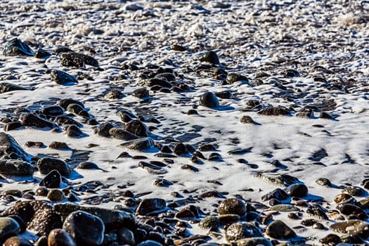 Stones in white foam on the beach coast or shore of ocean or sea