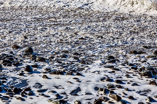 Foam and stones on the beach coast of ocean or sea