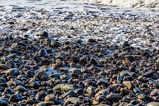 Stones in white foam on the beach coast of ocean or sea
