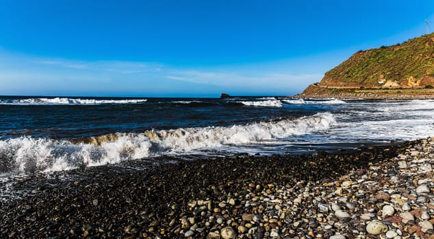 Wild stone beach on coast or shore panorama of the Atlantic ocean with waves and blue sky and skyline or horizon in Tenerife Canary island, Spain