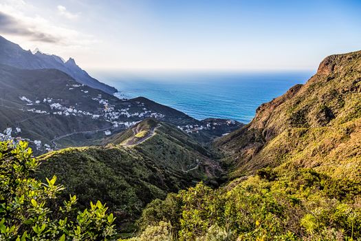 City or village and winding or serpantine road in green mountain or rock valley and clouds with horizon landscape near coast of Atlantic ocean in Tenerife Canary island, Spain