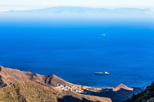 View from above from rock or mountain on ocean or sea with cargo ship. Island on background