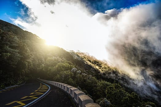 Asphalt road in mountains or rocks and sky with sun and sunlight and clouds over peak in Tenerife Canary island, Spain at sunset