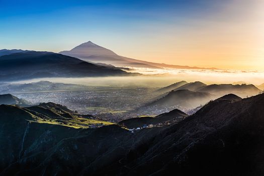 Sunset at evening in mountains and blue sky with fog or haze and Teide volcano on background in Tenerife Canary island, Spain at spring or summer