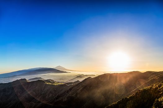 Sun with sunlight over mountains on blue sky with fog or haze and Teide volcano on background at evening sunset in Tenerife Canary island, Spain