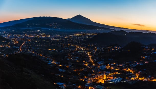 City with illumination after sunset at evening in mountains with blue sky and Teide volcano on background panorama landscape in Tenerife Canary island, Spain