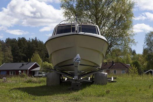 A boat on a trailer in front of some houses with a nice sky in the background