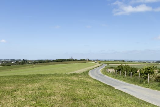 A long an winding road on a field with Mont St Michel in the background