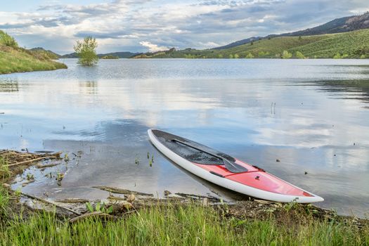 red SUP paddleboard with a paddle on a grassy lake shore - Horsetooth Reservoir near Fort Collins, Colorado