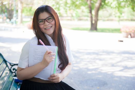 Student wearing glasses, holding a document. Sitting on a bench in the park.