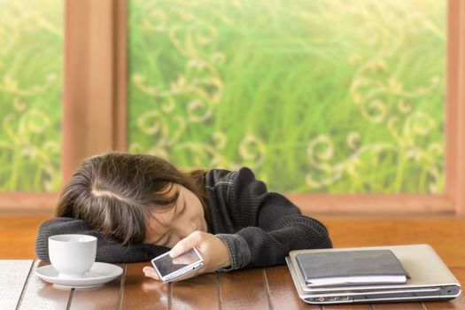 Tired asian girl sleeping at desk and hold smartphone in hand