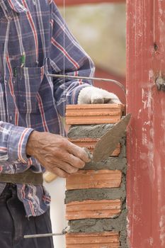 Bricklayer working in construction site of brick wall. Bricklayer putting down another row of bricks in site