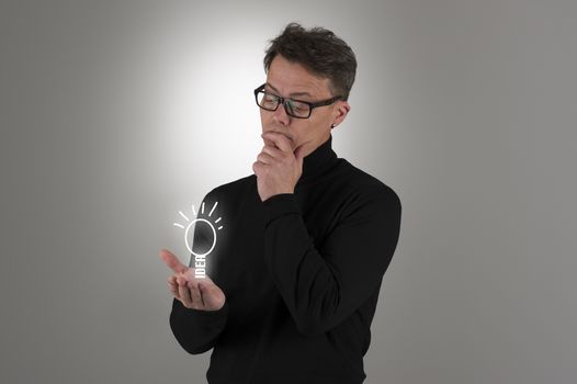 Conceptual image of a handsome man wearing nerdy glasses standing contemplating a bright idea or pondering the solution to a problem with a sketched shining light bulb balanced on his hand