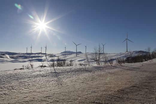 Windturbines on a hill with some sunshine in the background