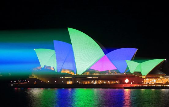 SYDNEY, AUSTRALIA - MAY 25, 2015;   Light beams stream onto the iconic landmark, the Sydney Opera House illuminating it roof sails in vivid green blue and pink during Vivid Sydney annual festival event.