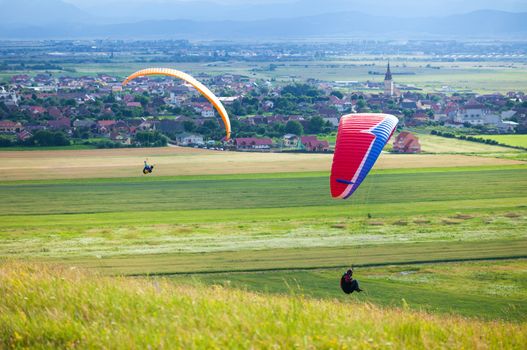 Paragliders flying over green fields with typical romanian village on background