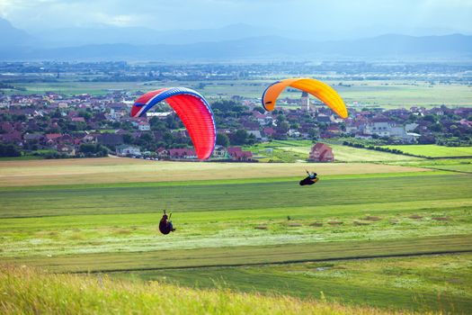 Paragliders flying over green fields with typical romanian village on background