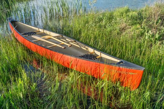 red canoe with wooden paddles on a grassy lake shore