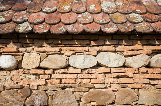 Rustic wall with layers of different comstruction materials - sandstones, bricks, river stones and roof tiles