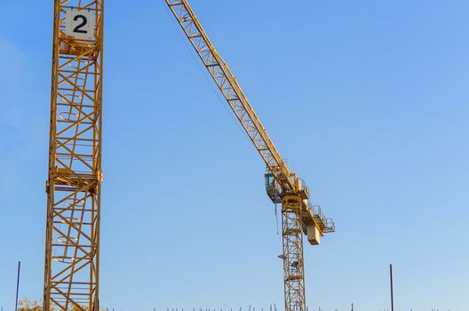 Two Construction cranes on a construction site against a blue sky.