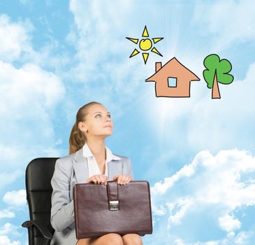 Business woman in skirt, blouse and jacket, sitting on chair and holding briefcase imagines house with tree. Against background of blue sky and clouds