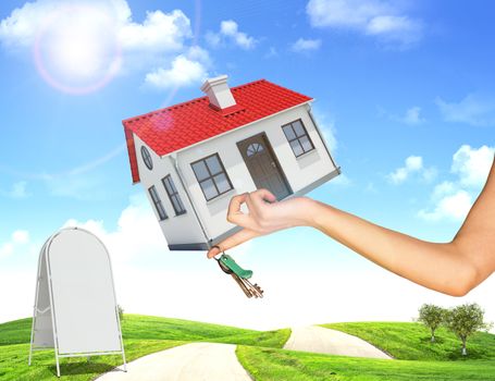 Hand holding house and bunch of keys. In background, green hills with grass and roads. Near with house sidewalk sign. Blue sky