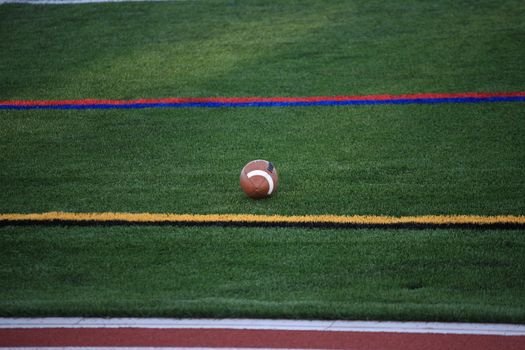 A football game ball rests on a turf grass field in between sideline markers.
