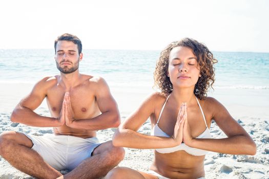 Happy couple doing yoga beside the water at the beach